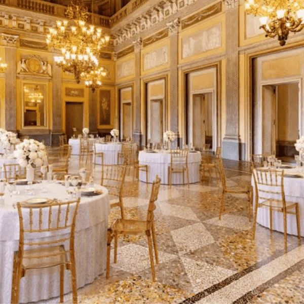 Vista del salón del Palacio de Mafra en Portugal con mesas redondas, sillas doradas y decoración clásica.