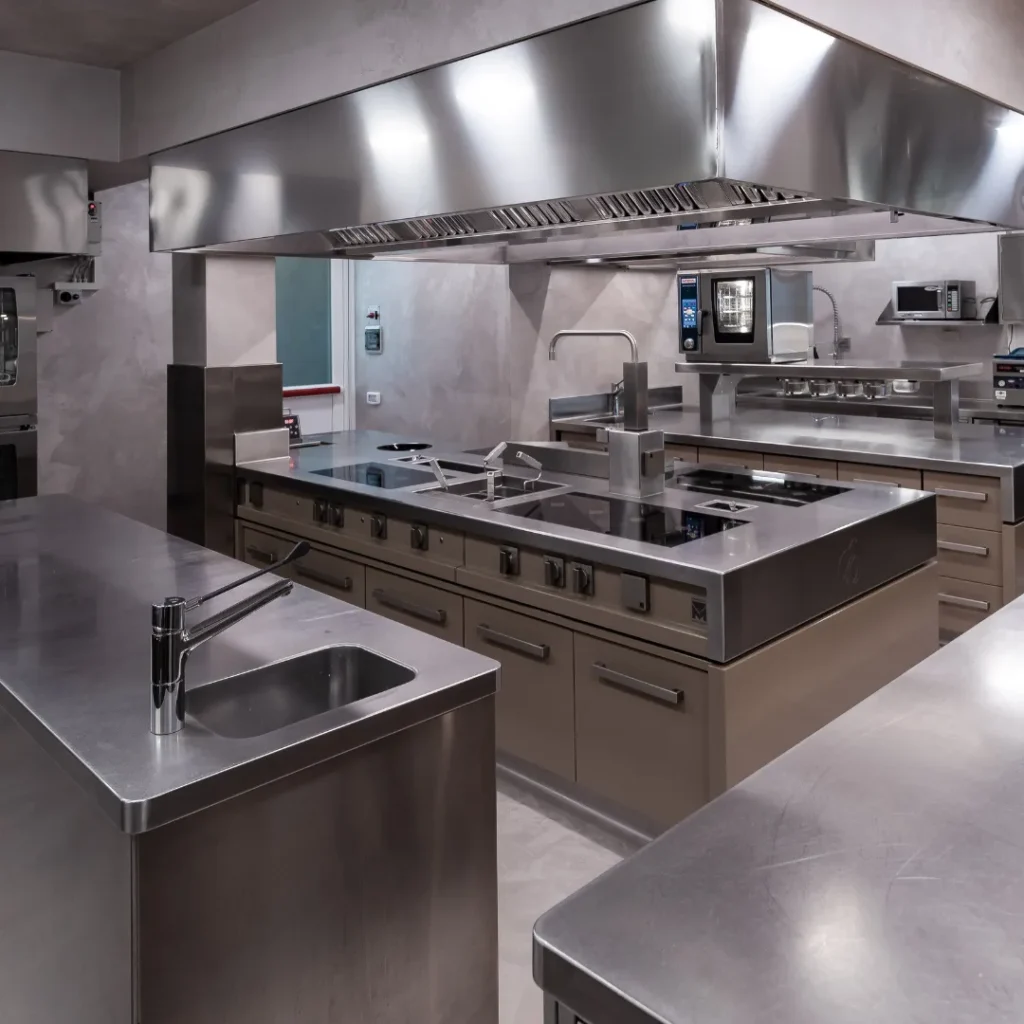 Cocina profesional de alta gama con encimeras y campanas extractoras de acero inoxidable, fregaderos integrados y módulos de almacenamiento beige.