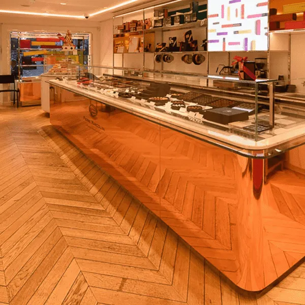 Interior de la chocolatería Pierre Marcolini en Londres, con mostrador dorado brillante y vitrinas de chocolates.