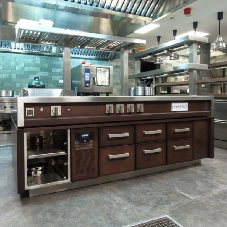 Estación de cocina Pasztell con encimera de acero inoxidable y frente de madera oscura, rodeada de equipo profesional.